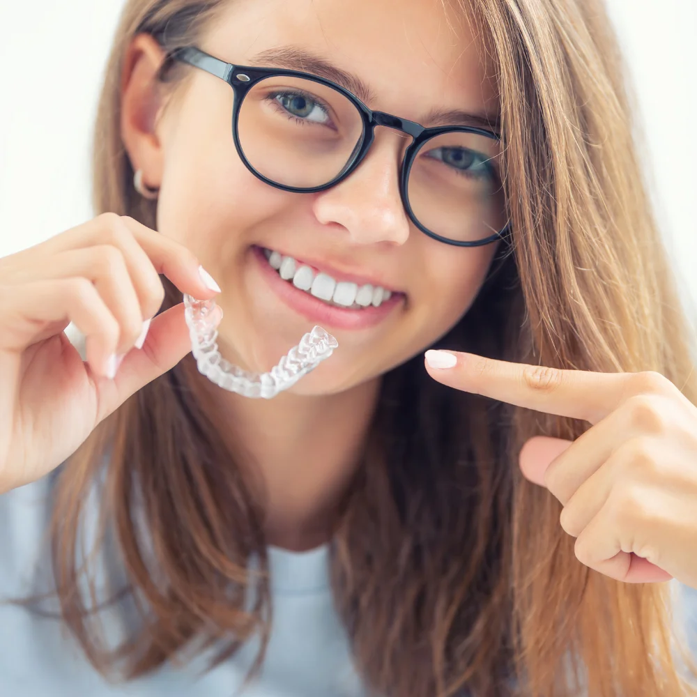 Teen patient smiling and holding a clear dental aligner, demonstrating orthodontic treatment option at Hanlon Creek Dental in Guelph, Ontario.