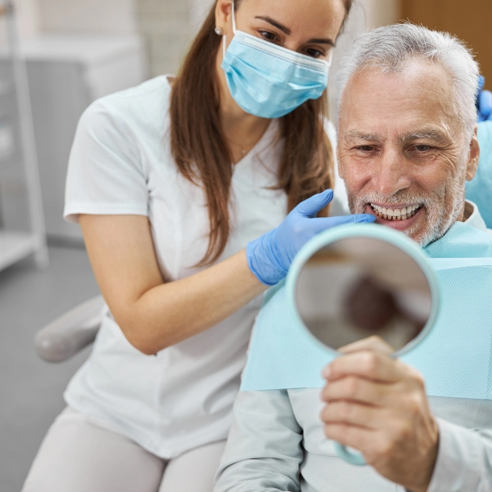 Senior patient smiling and looking in the mirror after dental implant treatment at Hanlon Creek Dental in Guelph, ON