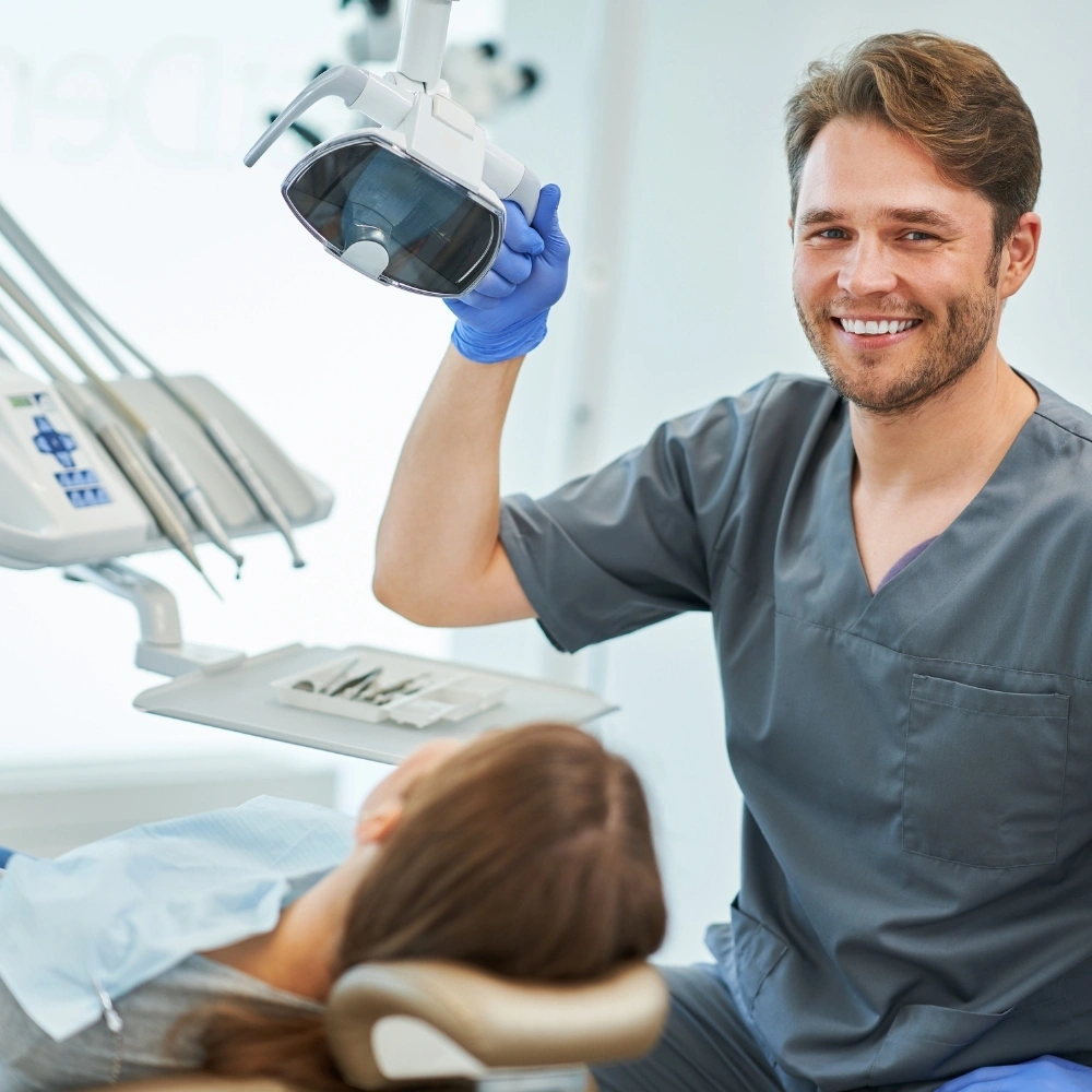 Dentist smiling while preparing treatment light above patient in dental chair at Hanlon Creek Dental in Guelph, ON.