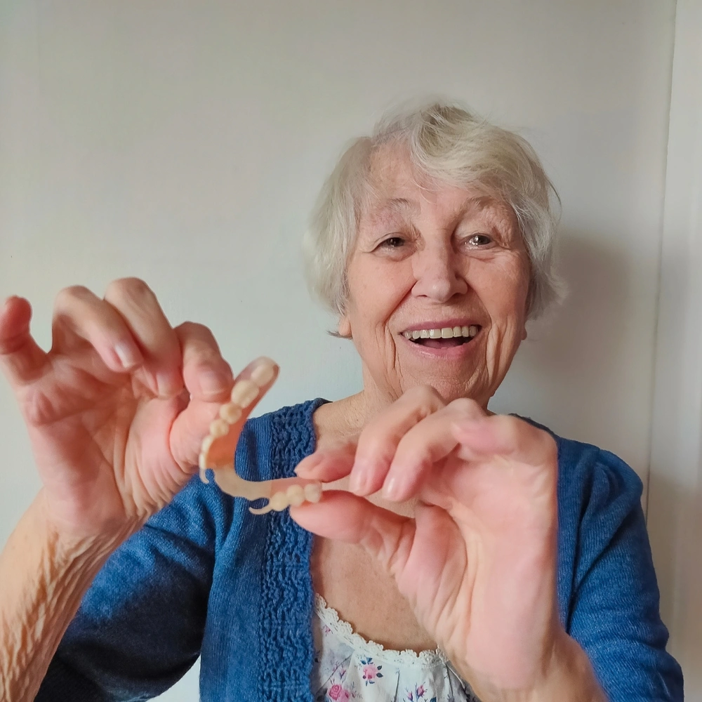 Senior patient smiling while holding removable dentures after fitting at Hanlon Creek Dental in Guelph, ON
